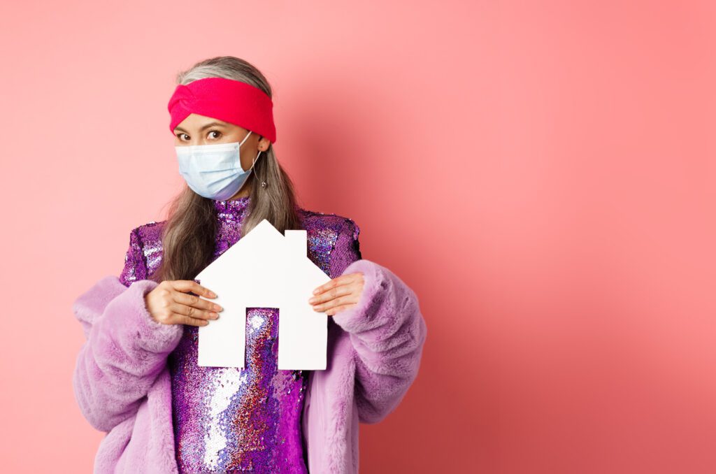 covid real estate concept stylish asian senior lady shiny dress showing paper house model rec edited